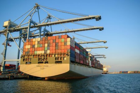 Large cargo ship docked at busy commercial port with shipping containers