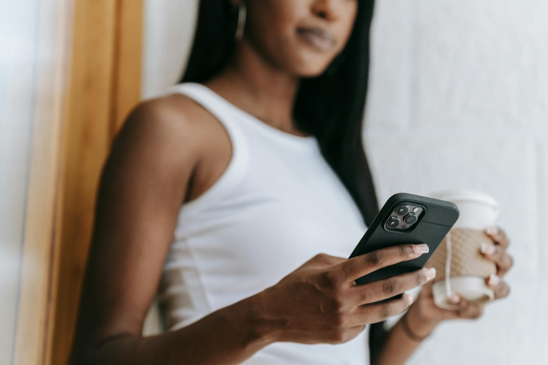 Person using mobile phone app while holding coffee cup, representing digital cafe subscriptions