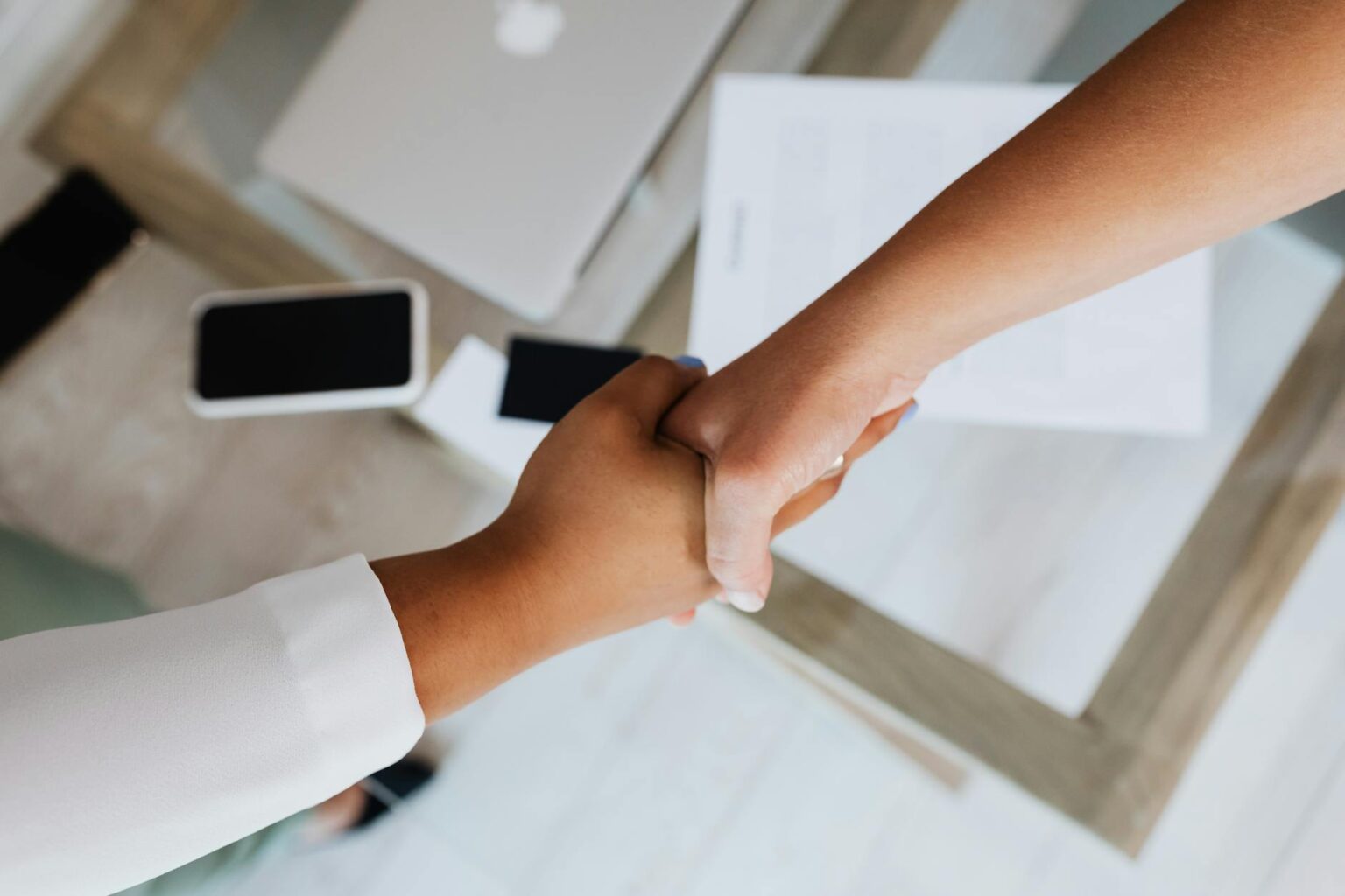 Major Credit Card Companies Are Acquiring Buy-Now-Pay-Later Startups Two business professionals shaking hands over acquisition documents and financial paperwork